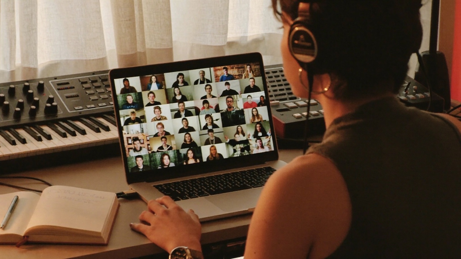 An artist in their home studio, headphones on, joining a live online session on a laptop full of other artists