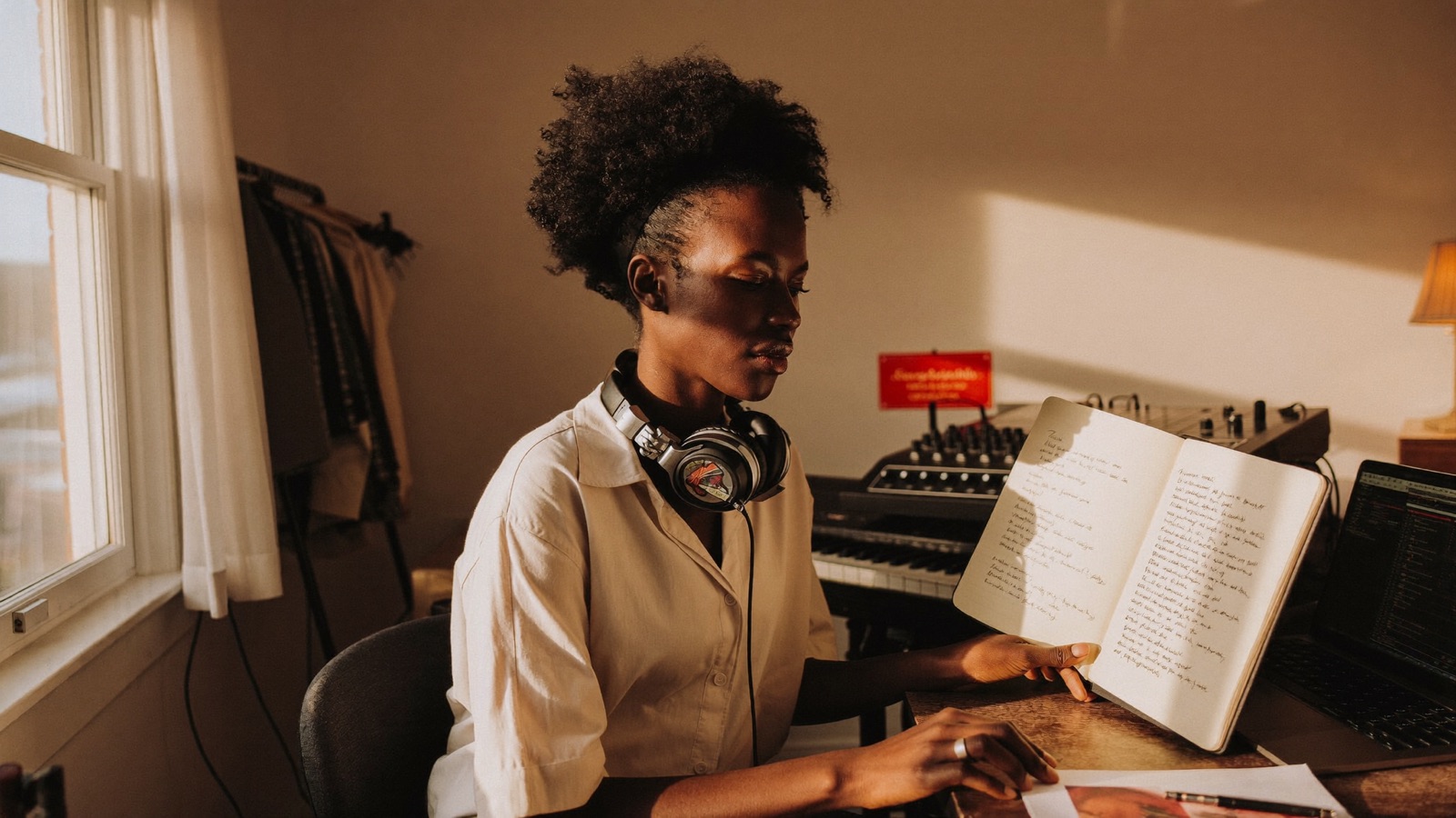 An artist working on a song at a home studio desk, notebook open beside the keyboard
